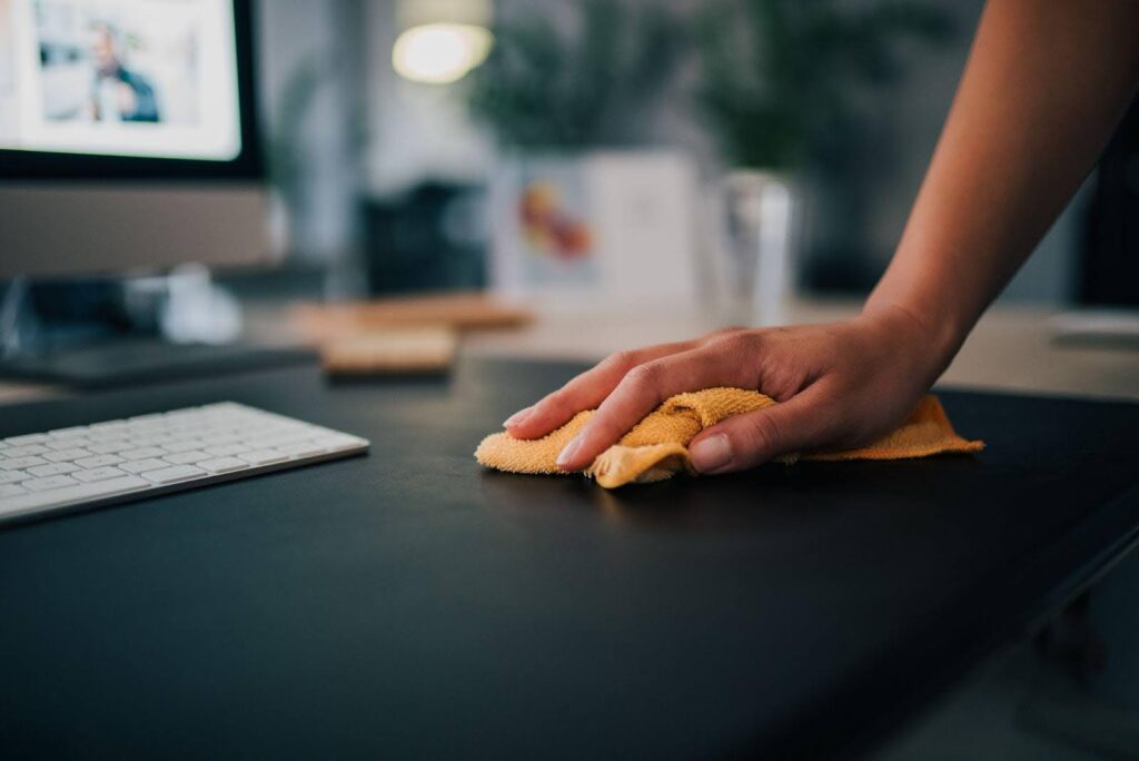 A hand wipes a dark desk with a yellow cloth