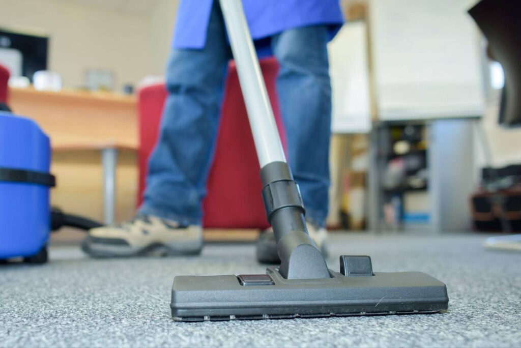 Person vacuuming a carpet in an office