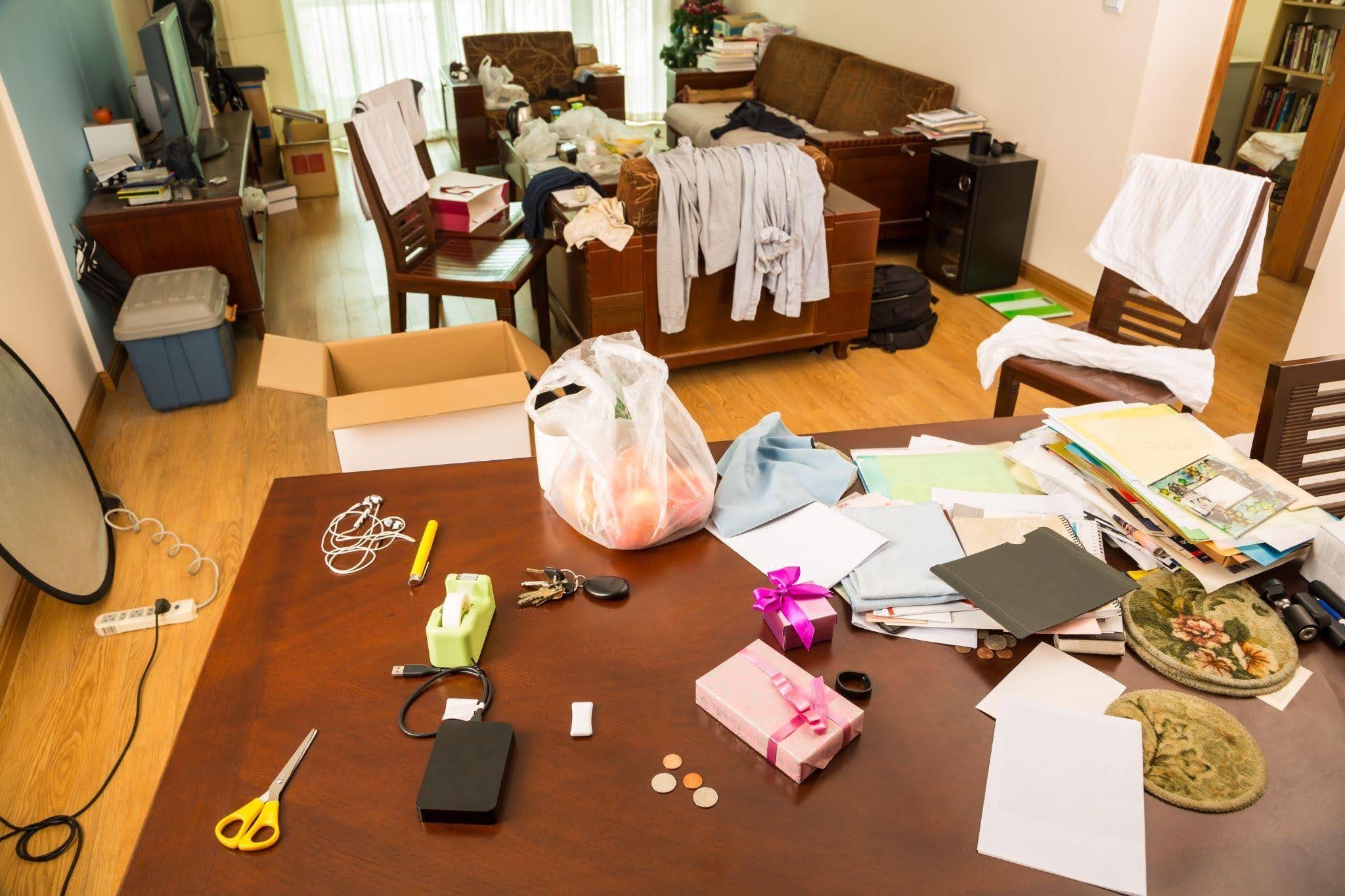 A messy living room with a table and chairs filled with disarray and various items strewn about the space