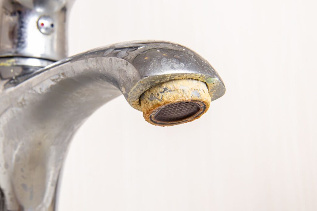Close-up of a chrome faucet spout covered in heavy limescale and hard water buildup