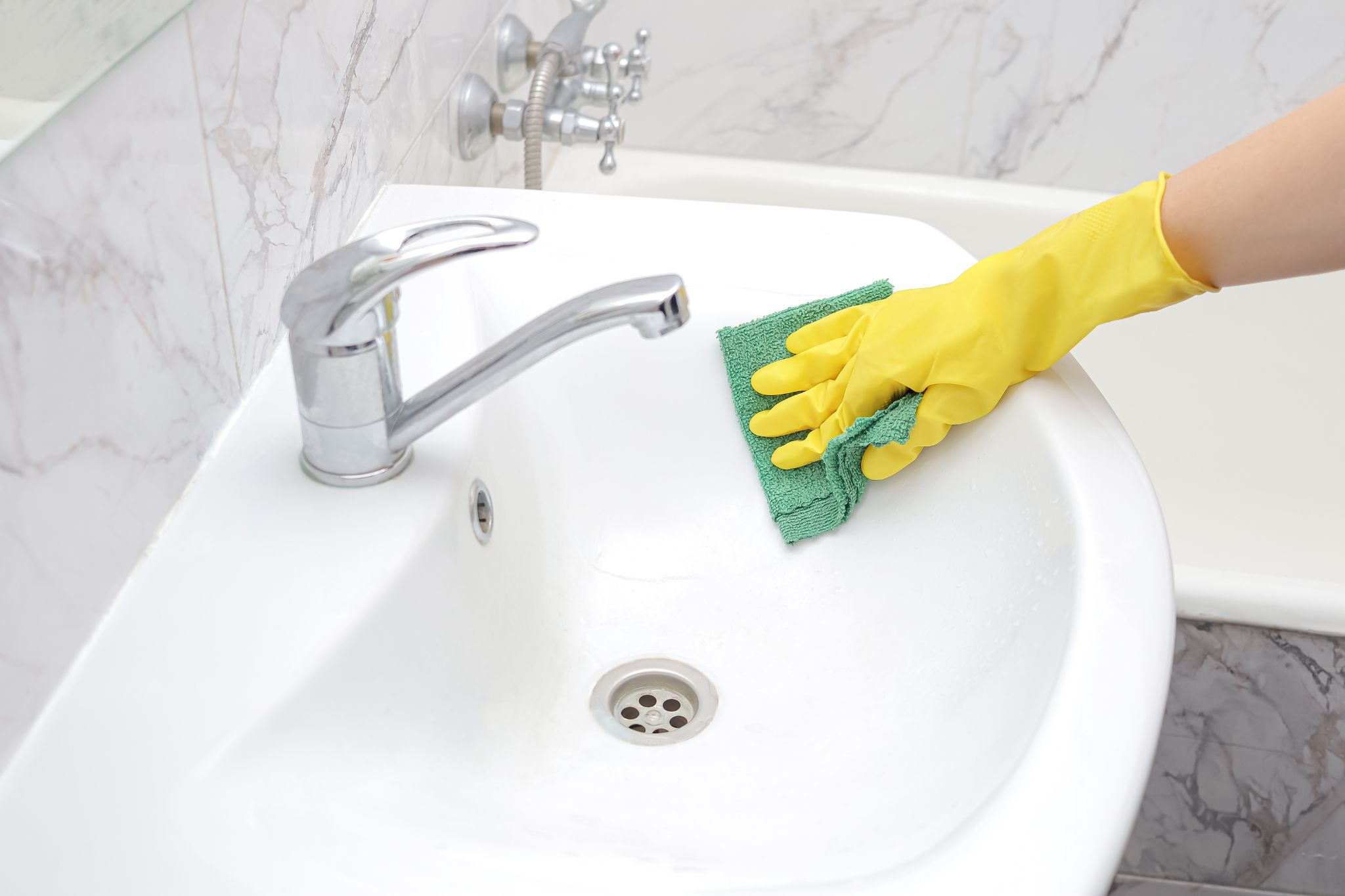 Gloved hand wiping down a white bathroom sink with a cloth