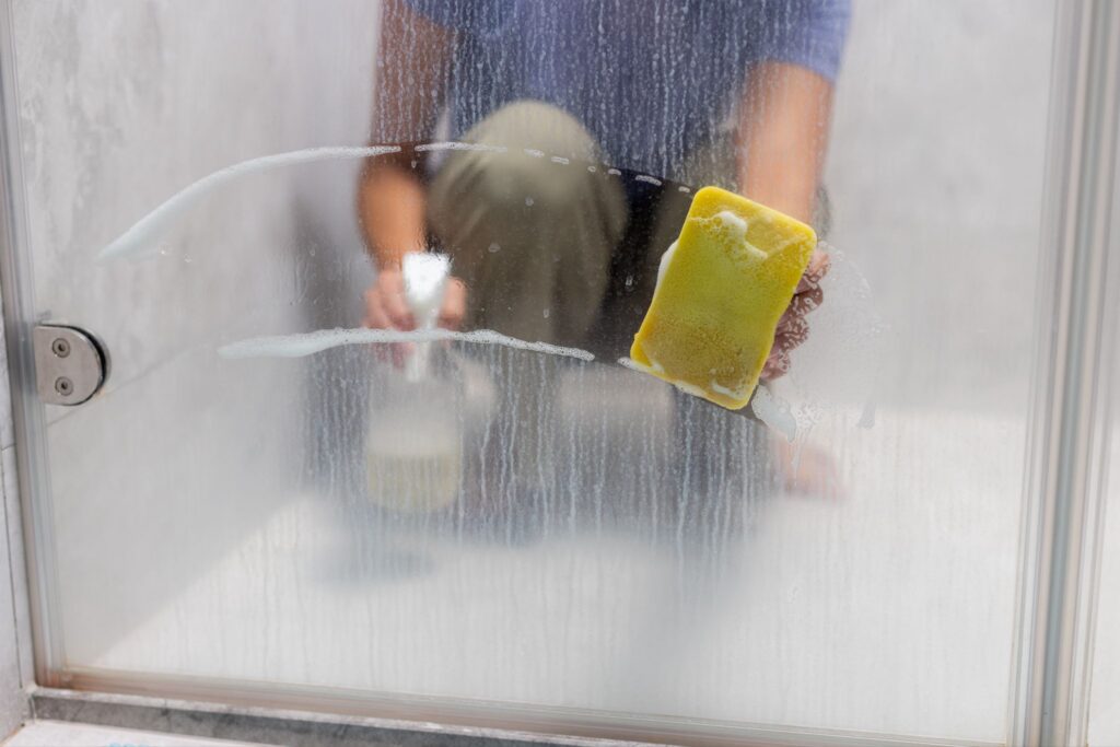 Person scrubbing soapy glass shower doors with a sponge